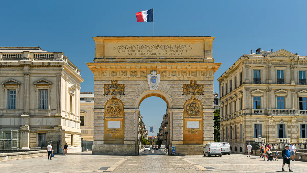 L'arc de triomphe de Montpellier, pierre dorée sous un ciel d'été.