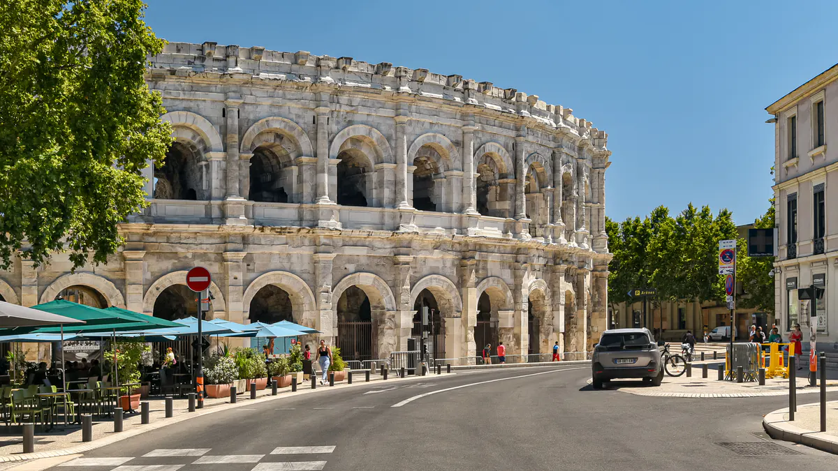 Les arènes de Nîmes en plein été, au bout d'une rue bordée de terrasses.